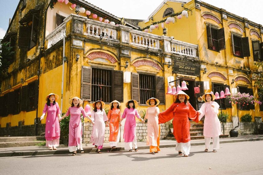 A group of women in traditional dresses and hats walking in front of a yellow building with arched windows and a balcony. 5