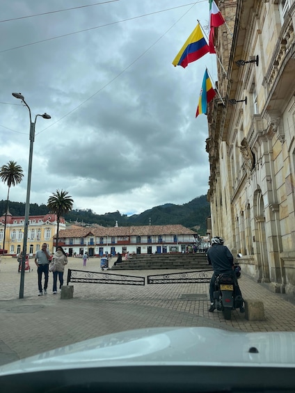 A cobblestone plaza with people, a parked motorcycle, and buildings with flags. 4