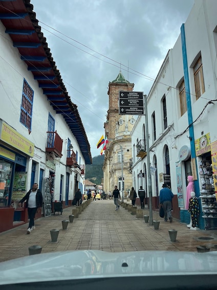 A cobblestone street lined with buildings, a clock tower, and a signpost with directions to various landmarks. 5