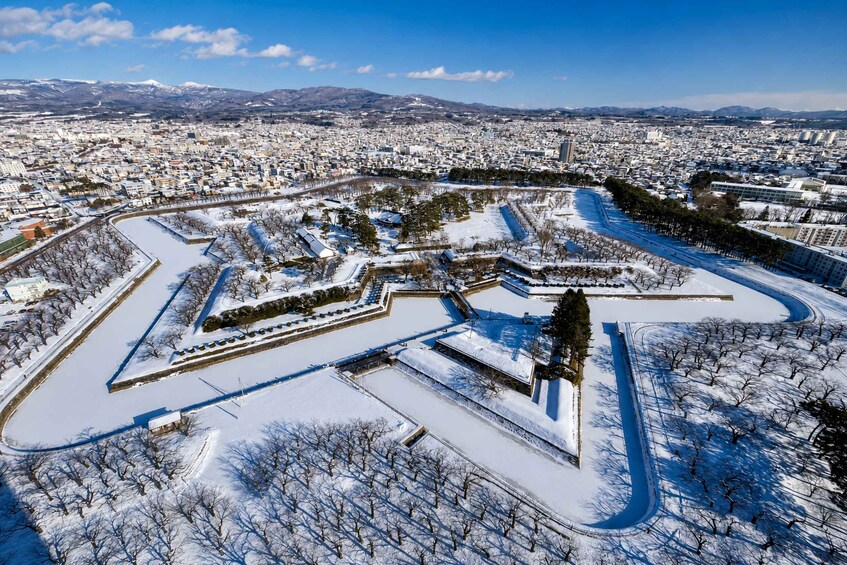A snow-covered park with geometric pathways and a cityscape in the background. 4