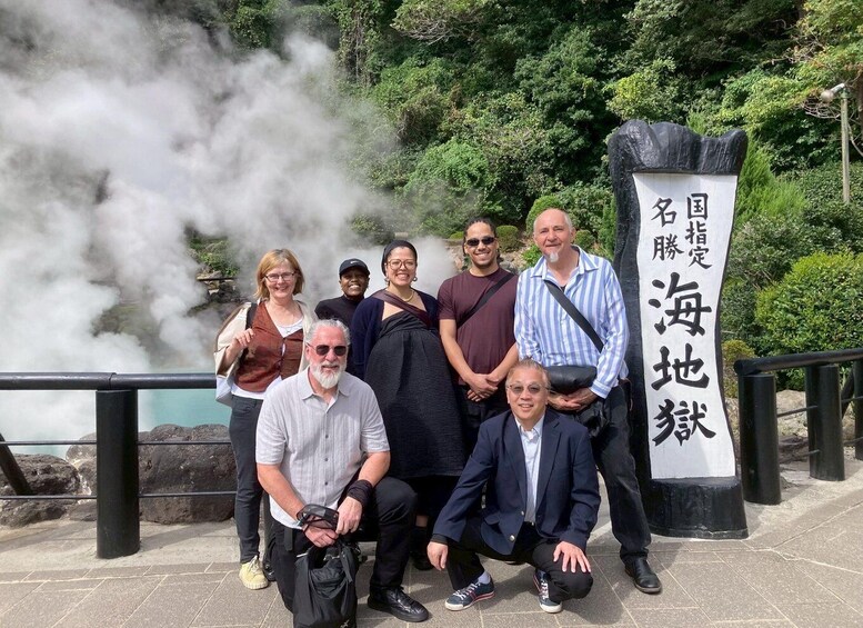 A group of people posing in front of a sign with Japanese characters, with steam rising in the background. 1
