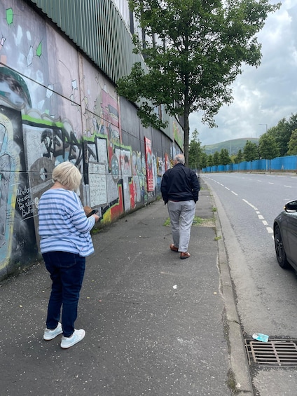 Two people walking along a graffiti-covered wall beside a road. 3
