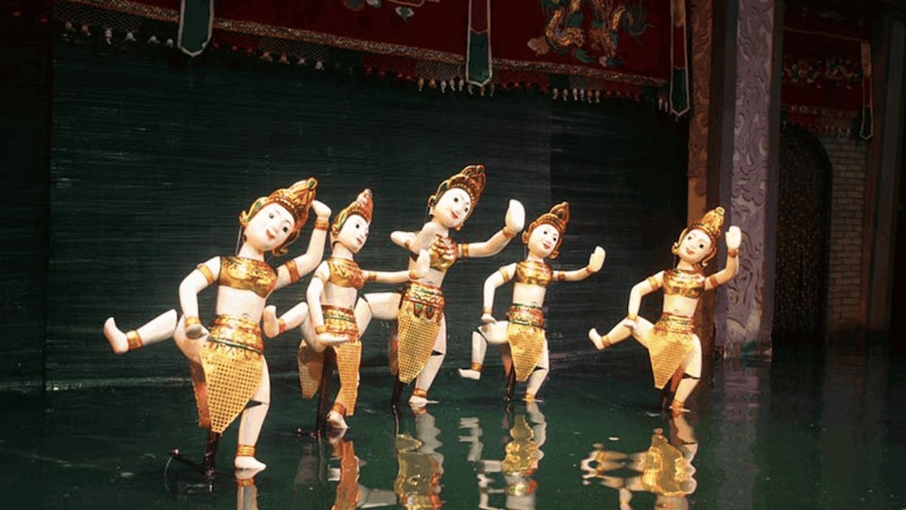 A group of dancers in traditional costumes performing on a stage with a dark backdrop and ornate decorations. 4
