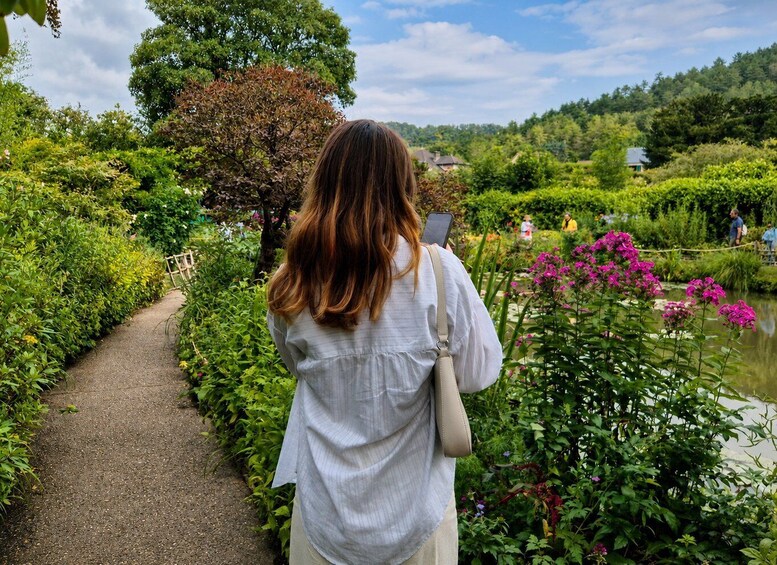 En person går på en sti gennem en have med et bassin og lyserøde blomster. 4