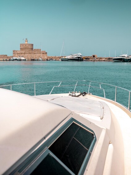 A boat docked near a historic fort and several yachts in the background. 4