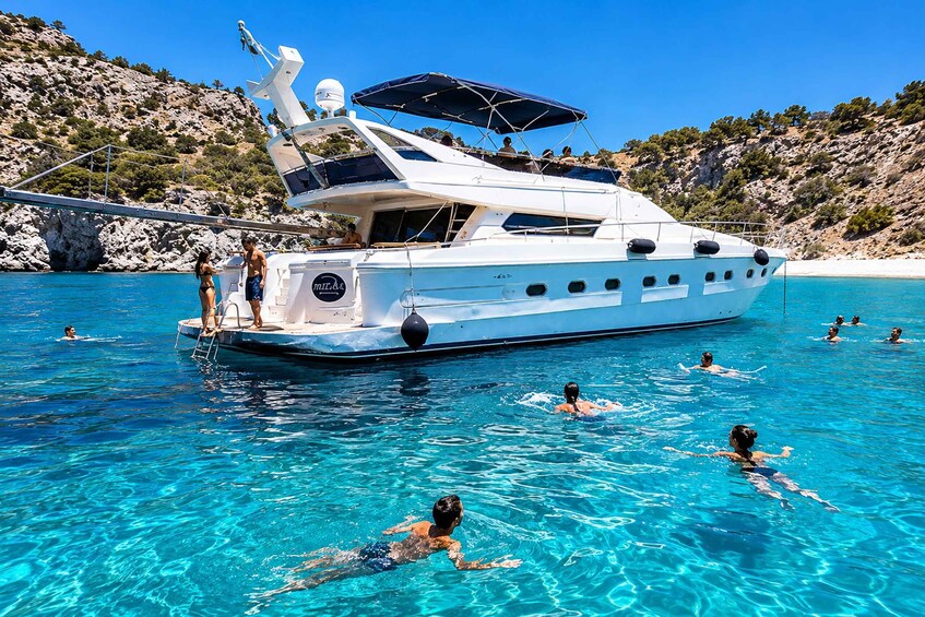 A yacht docked at a clear blue beach with people swimming in the water. 1