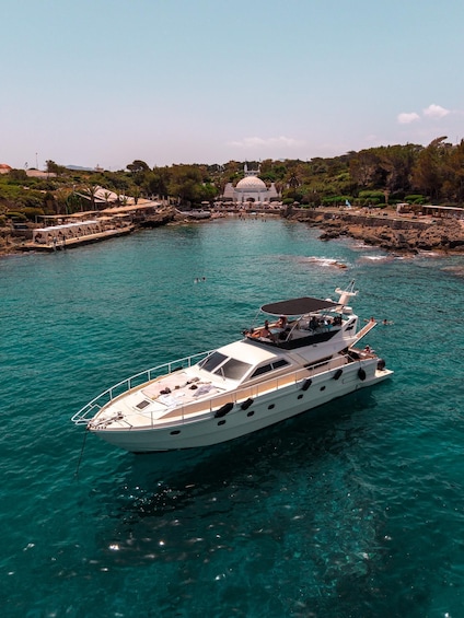 A white yacht anchored near a rocky shore with a dome-shaped building in the background. 2