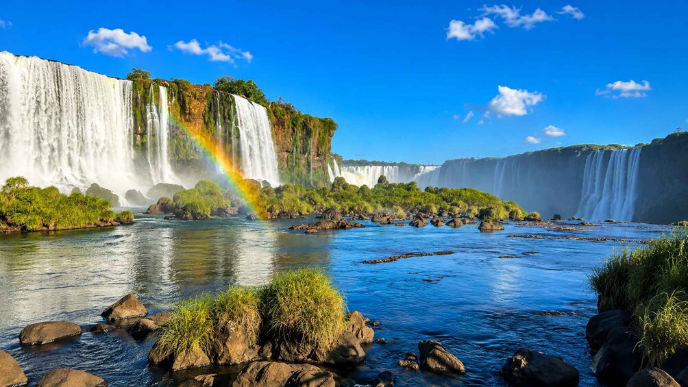 A large waterfall with a rainbow, surrounded by greenery and rocks. 5