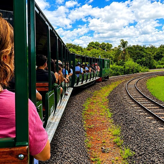 A green train with passengers traveling along a curved track surrounded by greenery. 3