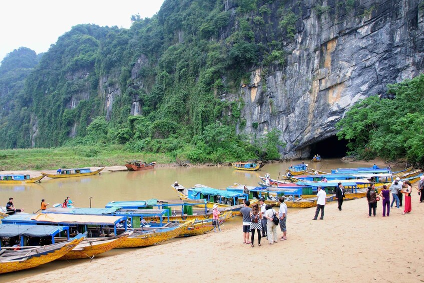 A riverbank with boats docked and people standing on the sand. 1