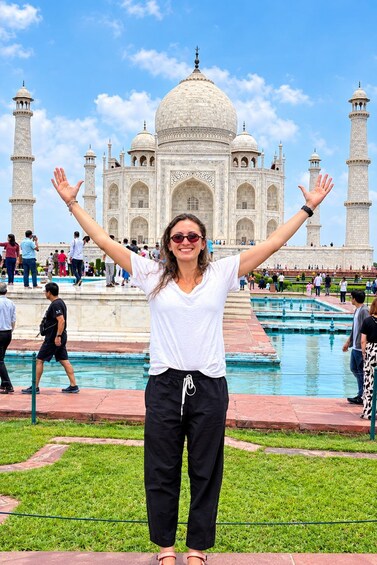 A person standing in front of the Taj Mahal with arms raised, surrounded by a pool and visitors. 1