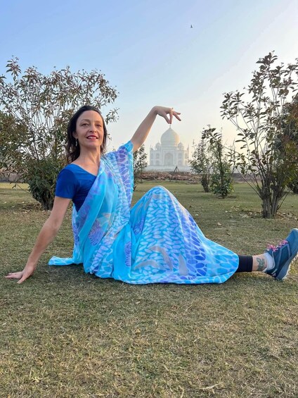 A person in a blue saree sitting on grass with the Taj Mahal in the background. 2