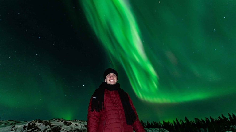 Una persona de pie sobre un paisaje nevado bajo un cielo nocturno con aurora boreal verde. 3