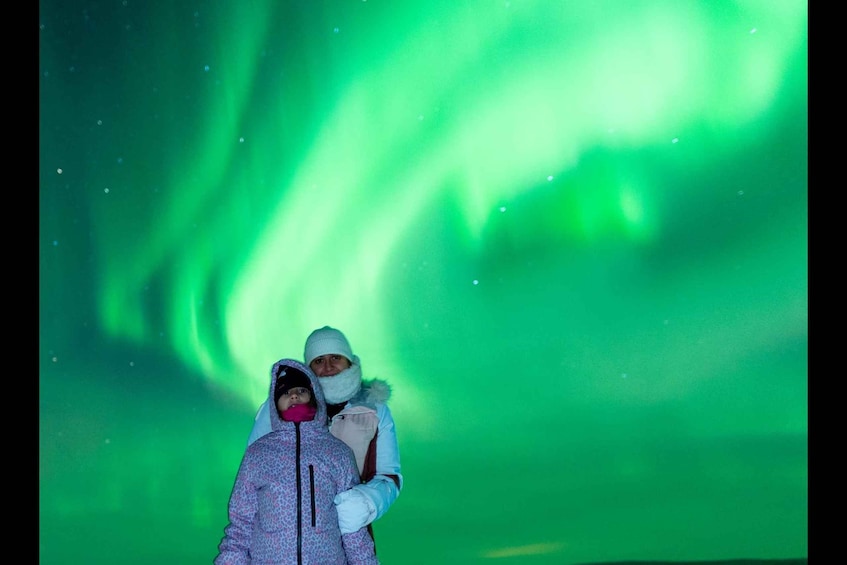 Dos personas frente a un espectáculo de aurora verde. 4