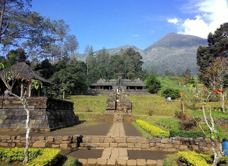 A stone pathway leading to a traditional building surrounded by lush greenery and mountains in the background. 2