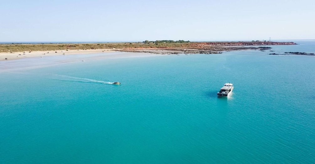 A boat moving through a turquoise sea with a sandy beach and rocky outcrops in the background. 2