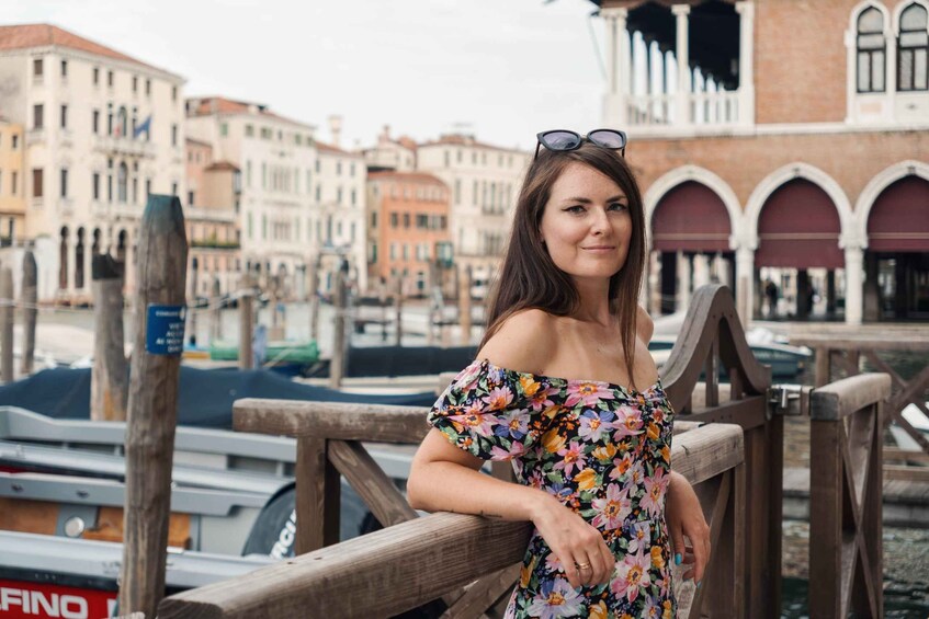 A woman in a floral dress standing on a wooden bridge with Venice's historic buildings in the background. 4