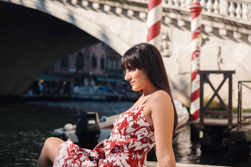 A woman sitting by a canal with a bridge in the background. 5