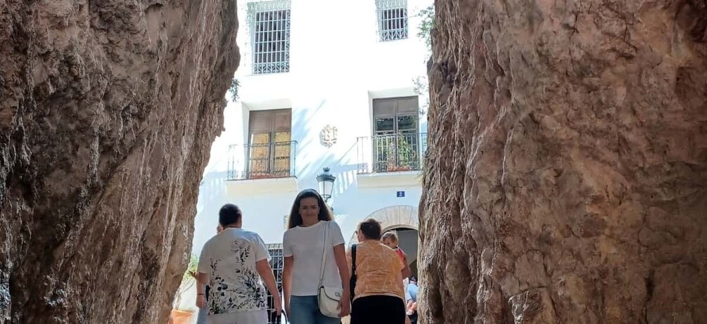 A group of people walking through a rocky archway towards a building with balconies. 4