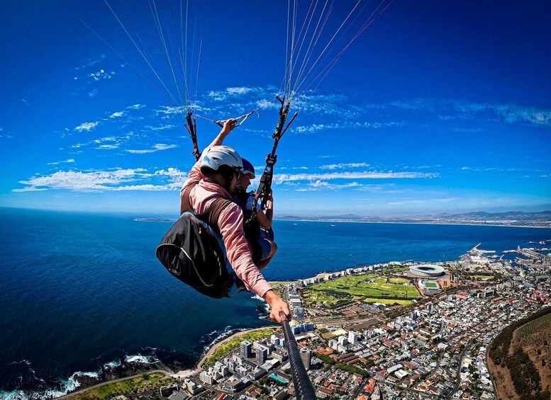A paraglider flying over a coastal city with a clear view of the ocean and urban landscape below. 1