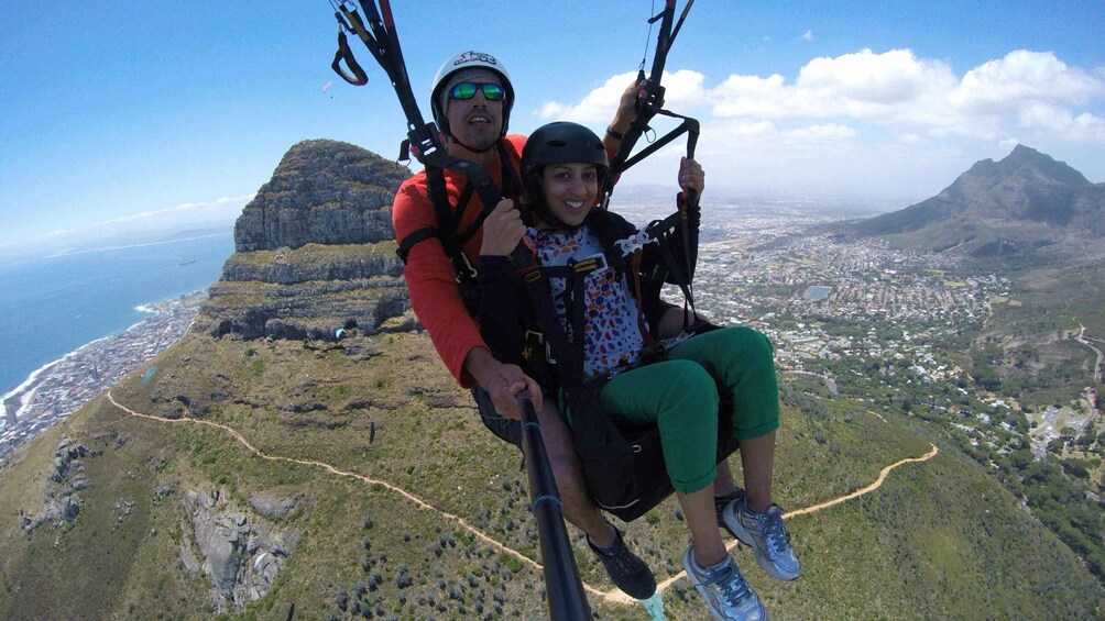 Two people on a tandem paragliding flight over a coastal landscape with a city below. 2