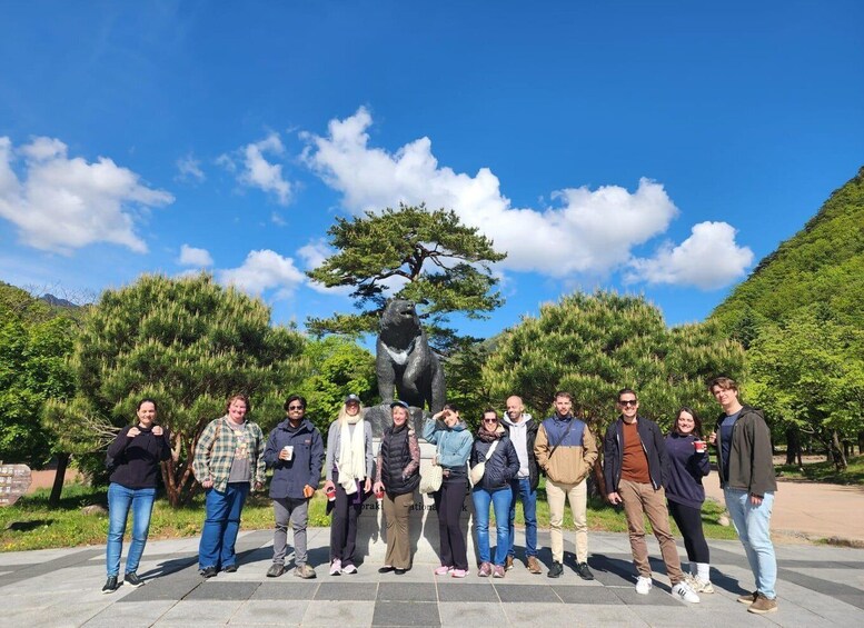 A group of people standing in front of a large tree sculpture with a bear figure. 4