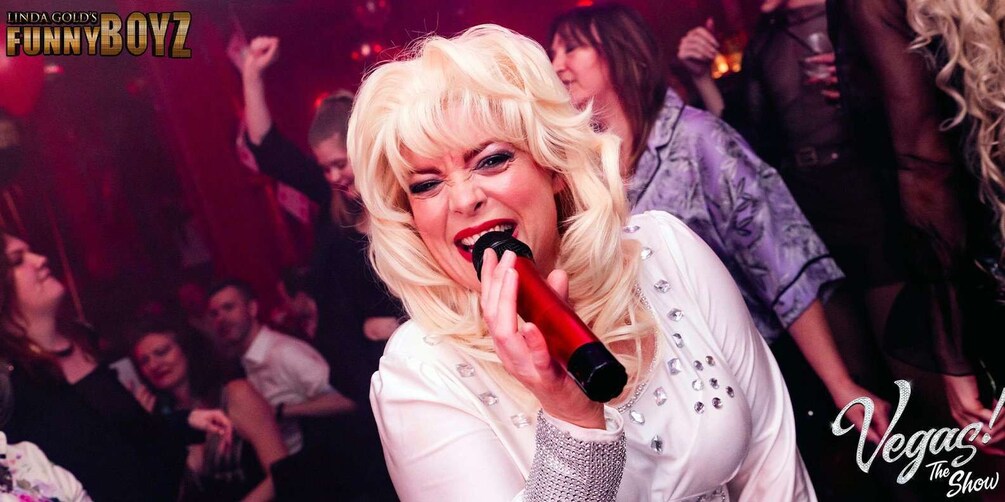 A person holding a microphone, dressed in a white outfit with sequins, at a lively event. 3