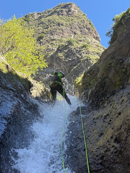 A person rappelling down a rocky cliff with water splashing around. 2
