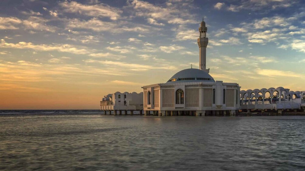 A mosque with a tall minaret and a dome, situated on stilts over water. 1