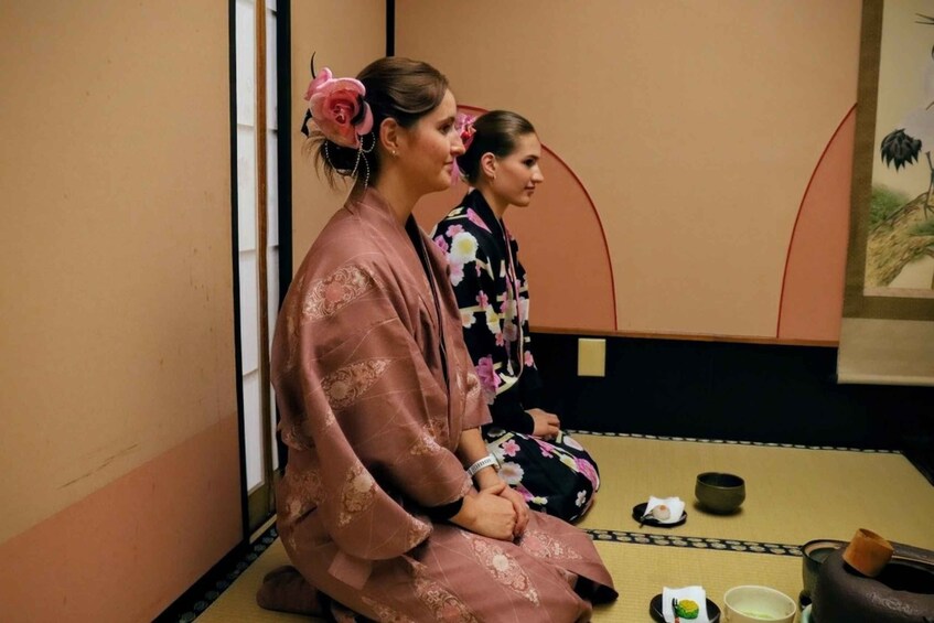 Two individuals in traditional Japanese attire sitting on tatami mats with a tea set in front of them. 3