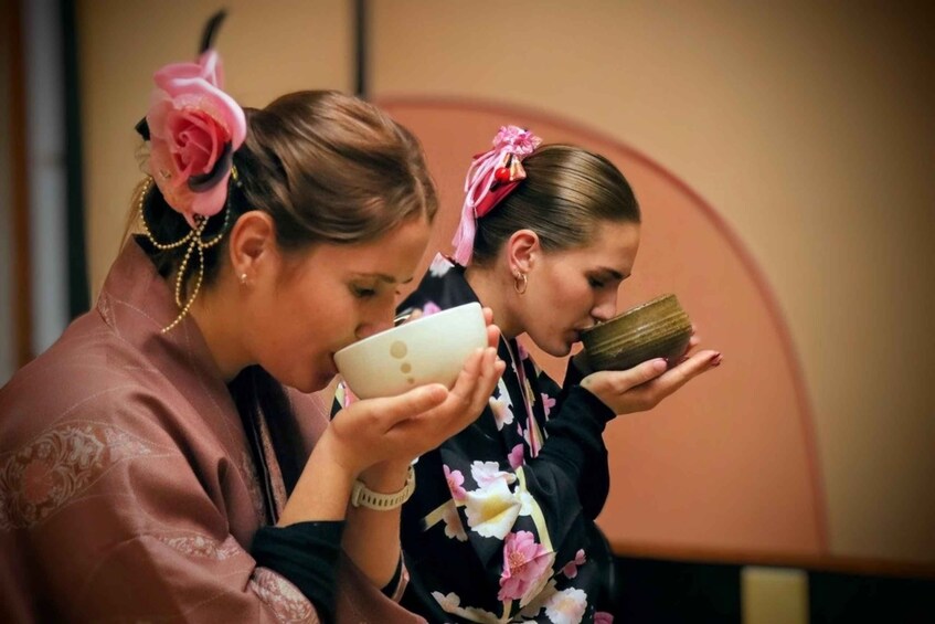 Two individuals in traditional attire with floral patterns, one holding a white object and the other holding a brown object. 1