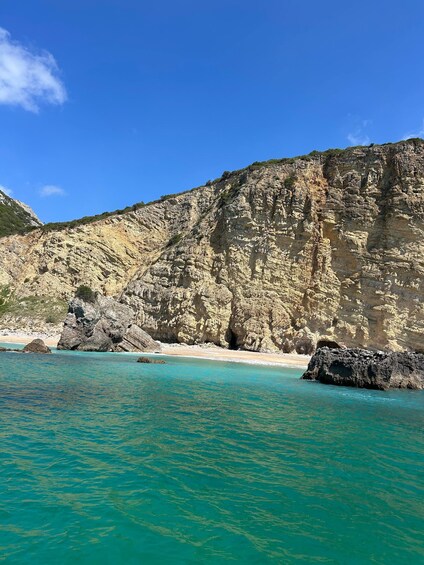 A coastal landscape with clear turquoise waters, rocky cliffs, and a sandy beach. 1
