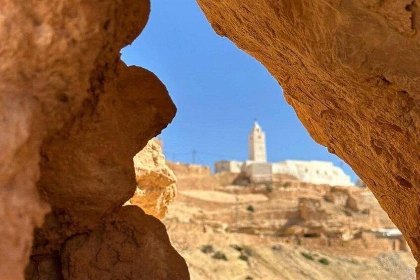 A rocky landscape with a prominent rock formation in the foreground and a building with a tower in the background. 1