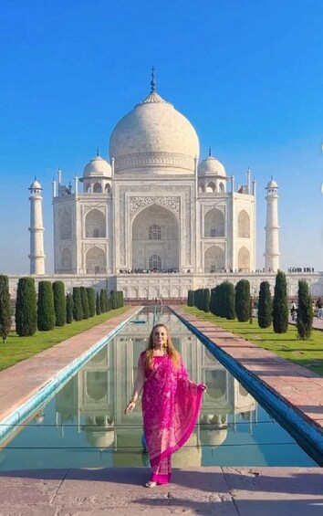 A person in a pink saree standing in front of the Taj Mahal. 2