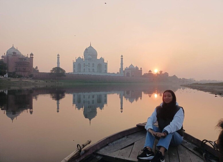 A person sitting on a boat near the Taj Mahal, with its reflection in the water and the sun setting in the background. 3