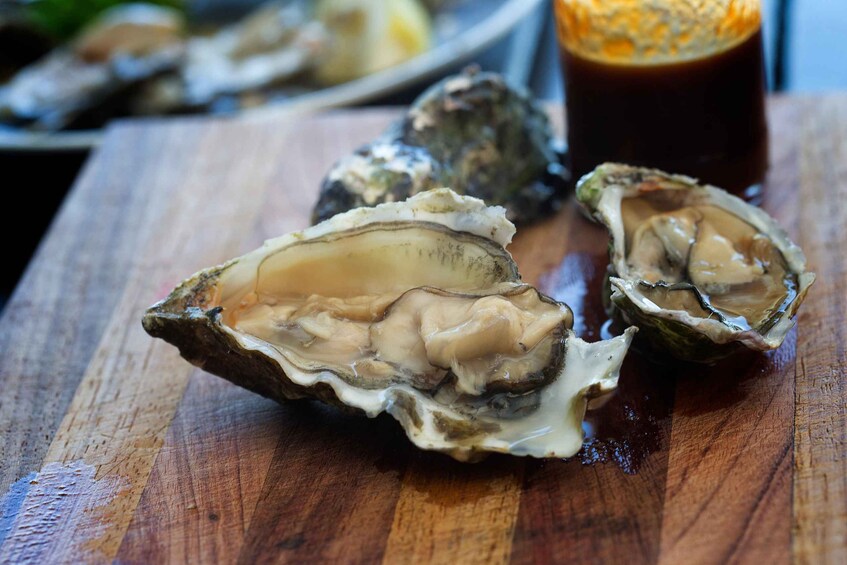 Oysters on a wooden board with a glass of dark liquid, possibly a sauce, in the background. 2