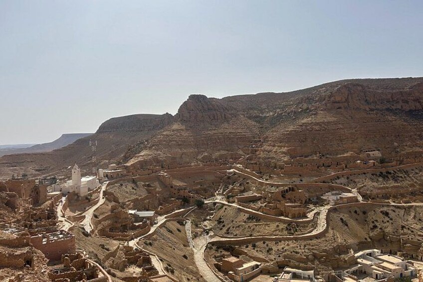 A rugged landscape with a white church, winding roads, and terraced fields. 1