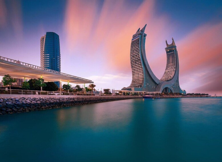 A waterfront with two distinctive buildings, one with a curved design and another tall, cylindrical structure. 1