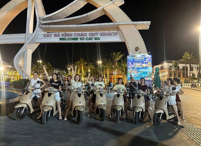 A group of people on scooters in front of a large illuminated sign with text. 1