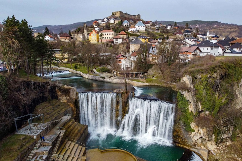 A waterfall cascading into a river, surrounded by a town with colorful houses and a castle on a hill. 5
