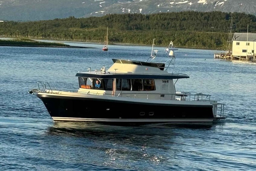 Un barco blanco y negro llamado 'Targa 46' sobre aguas tranquilas, con una orilla cubierta de bosque y montañas al fondo. 5