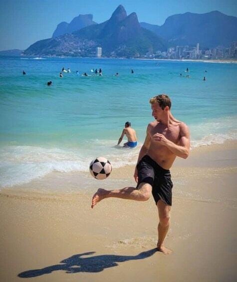 A man playing soccer on a beach with mountains in the background. 4