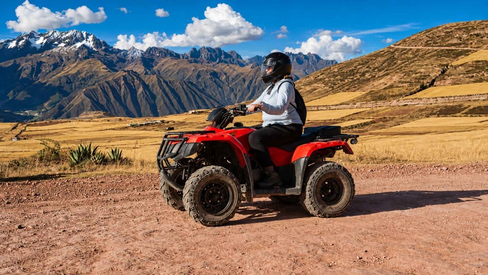 A person riding a red ATV on a dirt road with mountains in the background. 5