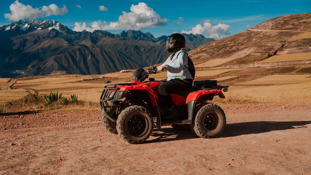A person riding a red ATV on a dirt path with mountains in the background. 1