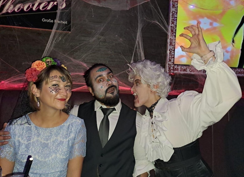 Three people posing in front of a Halloween-themed backdrop with a spider web and a sign that reads "Große Freiheit." 2