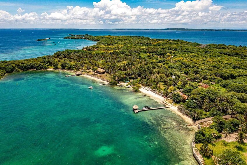 An aerial view of a tropical island with clear turquoise waters, a dock, and a beach area surrounded by dense greenery. 4