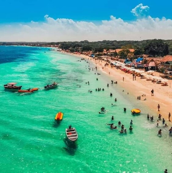 A beach with clear turquoise water, several boats, and people swimming and sunbathing. 1