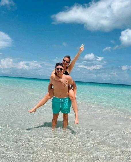 A person carrying another on their back in shallow, clear turquoise water. 3