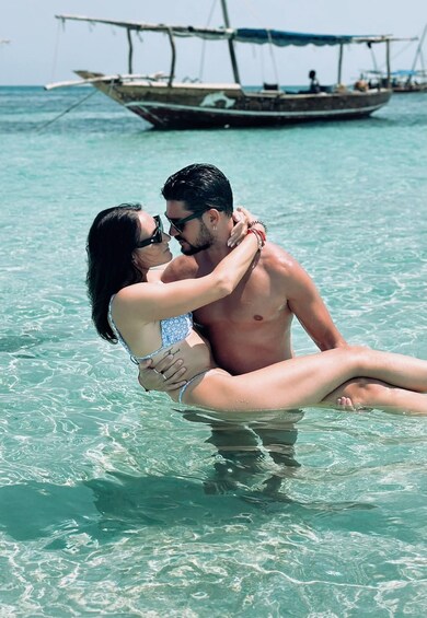 A couple embracing in clear turquoise water with a boat in the background. 5