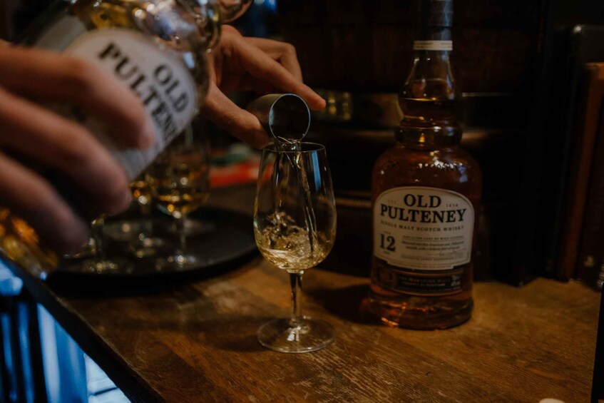 A bottle of Old Pultney 12 whisky and a glass on a wooden surface. 1